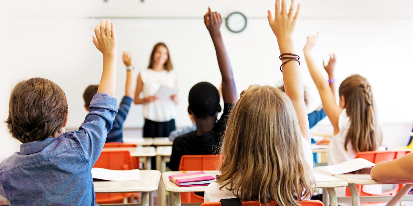 Enfants qui lèvent la main dans une classe à l'école